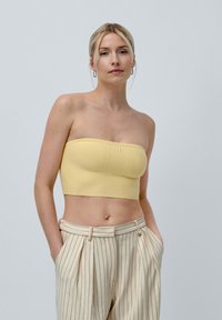 Yellow strapless crop top with a textured finish and seam detailing, paired with cream and brown striped high-waisted trousers.