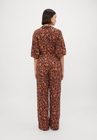 Lepardo print jumpsuit met een bruin en zwart patroon, korte mouwen, een strik taille en wijde broekspijpen. Lichtgewicht stof met een gladde textuur.
