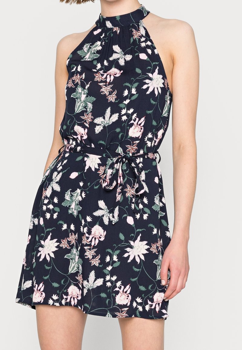 Hemdblusenkleid in Marineblau mit Blumenmuster, featuring einen Halterneck, verstellbaren Taillengürtel und einem weichen, strukturierten Stoff mit rosa und grünen Blumenmustern.