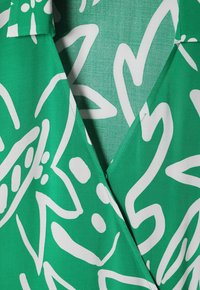 Grüner Stoff mit großem weißen abstrakten Blumenmuster, mit tailliertem Ausschnitt und glatter Textur, ideal für Freizeitanlässe.