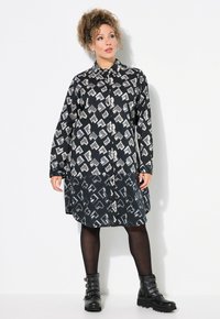 Abito camicia a maniche lunghe in nero e grigio con un motivo astratto, chiusura con bottoni sul davanti e orlo curvo. Indossato con stivaletti neri alla caviglia.