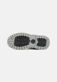 Zwarte en grijze rubberen schoenzool met diepe groeven en een gestructureerd patroon. Heeft een ronde grippad in het midden voor grip.