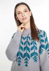 Grå sweater med teal-bladmønster, ribbet rund hals og lange ærmer. Blød tekstur med synlige strikkedetaljer og afslappet pasform.