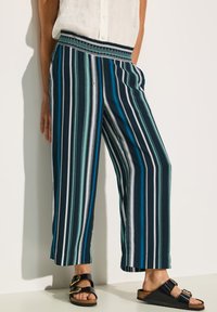 Pasiasty szerokie spodnie w kolorach granatowym, turkusowym i białym z elastycznym pasem, zdobionym wzorem. Gładki materiał o luźnym kroju.