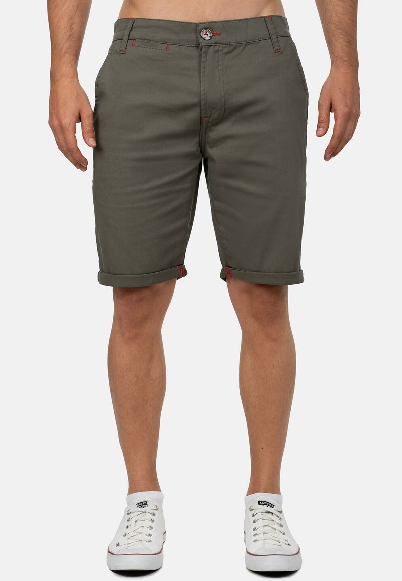 Khaki shorts met opgerolde pijpen, gemaakt van lichtgewicht stof. Kenmerken zijn rode stikselaccenten en een standaard knoopsluiting. Gecombineerd met witte sneakers.