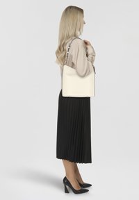 White leather shoulder bag with smooth texture, minimalist design, black accents, and a single adjustable strap, shown against a gray background.