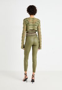 Olive zaļa tamborēta cropped džemperis ar garām piedurknēm, apvienots ar spīdīgiem olīvu legingiem, kuriem ir smalks raksts. Melni strappy papēži.