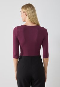 Burgundy fitted top with three-quarter sleeves, smooth texture, round neckline, styled with black high-waisted pants, minimal detail.