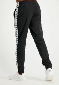 Pantalones atléticos negros con un ajuste slim y franjas laterales blancas con acentos de logo. Hechos de una tela suave, con una cintura elástica y puños en los tobillos.