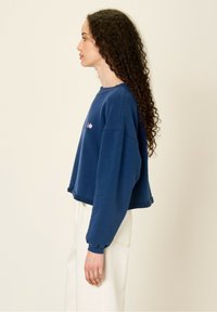 Felpa corta blu navy realizzata in tessuto morbido, con scollatura rotonda e maniche lunghe con polsini a coste. Dettaglio del logo multicolore.