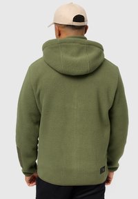 Grüne Fleece-Hoodie mit einer strukturierten Kapuze, strukturiertem Stoff und einem kleinen Logopatch am unteren Rücken. Lange Ärmel, eng anliegende Bündchen.