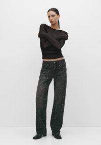 Top negru cu mâneci lungi, cu un design transparent și texturat și mâneci strâmte, asortat cu blugi negri largi, decorați cu studs albe.