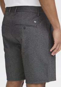 Gray textured shorts feature a straight cut, two back pockets, one with a button, and a branded accent on the waistband.