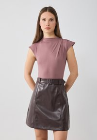 Top ajustado en color malva con mangas cortas y detalle fruncido, combinado con una falda de imitación de cuero marrón de cintura alta que incluye un cinturón y tiene forma de A.