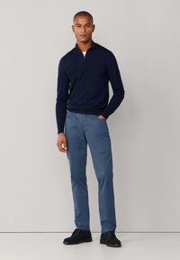 Granatowy sweter z suwakiem 1/4, jasnoniebieskie chinosy i ciemnoniebieskie zamszowe buty. Sweter ma ribbowany dół i dopasowany krój; spodnie mają gładkie wykończenie.