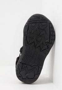 Black athletic shoe sole with a textured surface, featuring triangular and zigzag patterns for traction. Rounded toe and sturdy construction.