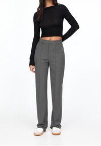 Grijze op maat gemaakte broek met een rechte pijp, in combinatie met een aansluitend zwart langemouwen top en witte sneakers met lichtbruine zolen.