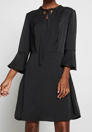 Sort knælængde kjole med 3/4 klokkeærmer og en nøglehuludskæring, bundet med en smal stofsløjfe ved kraven.