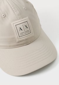 Bežna kapa od glatkog materijala s kvadratnom zakrpom s logom "AX" i "ARMANI EXCHANGE BLUE EDITION." Detaljno šivenje na viziru.