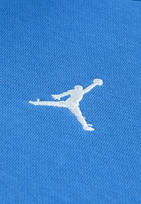 Fond en tissu bleu avec une silhouette brodée blanche d'une figure sautant en tenant un ballon de basket, présentant une texture lisse.