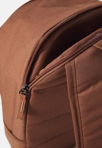 Bruine stoffen backpack met een textuur, voorzien van een ritssluiting, stevige schouderbanden en een schoon, minimalistisch ontwerp.