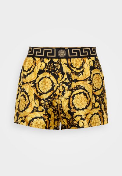 Černé šortky se žlutým květinovým vzorem, s černým a zlatým pasem s řeckým vzorem a výrazným emblémem Medusy uprostřed.