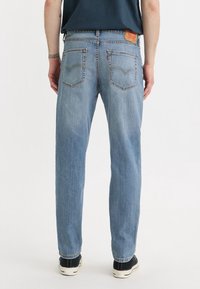 Světle modré džíny s rovnými nohavicemi a klasickým pětipočtovým designem kapes, vybavené koženou zadní nášivkou a kontrastními švy.