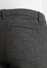 Pantalons à motif chevron gris avec un devant plat, comportant une poche arrière unique et une coupe classique ajustée. Tissu en mélange de laine texturé.