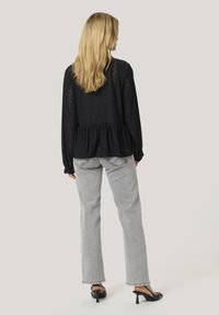 Black lace blouse with peplum waist, long sleeves, and open pattern design, paired with grey straight-leg jeans and black heeled sandals.