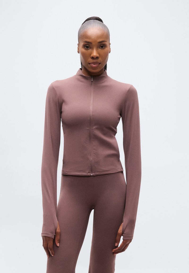 Ελαφρύ, μακρυμάνικο μπουφάν με φερμουάρ σε απαλό μωβ χρώμα. Λείο, ελαστικό ύφασμα με εφαρμοστή σχεδίαση και τρύπες για τον αντίχειρα στα μανίκια.