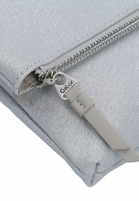 Silberne Clutch-Tasche aus Stoff mit einer glatten Textur, ausgestattet mit einem kontrastierenden Reißverschluss mit "Gabor"-Branding und einem grauen Ledertragegriff.