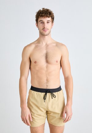 Shorts de bain beiges avec une taille élastique noire et un cordon de serrage. Tissu léger, coupe au genou, avec un petit détail de logo.