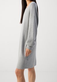 Robe pull en tricot gris à coupe décontractée, encolure large, manches longues et détails côtelés sur les épaules et les poignets. Texture douce.
