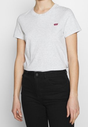 Osoba nosząca jasnoszarą koszulkę z krótkim rękawem z małym czerwonym logo Levi's oraz czarne spodnie z wysokim stanem.
