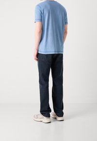 Jasnoniebieska bawełniana koszulka z krótkim rękawem, połączona z ciemnoniebieskimi dżinsami i beżowymi butami sportowymi. Prosty, casualowy design.