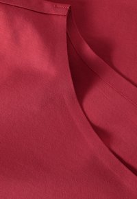 Lähedalt vaadatuna on kokku volditud punane kangas, millel on nähtav õmmeldud ääreosa ja sile tekstuur.