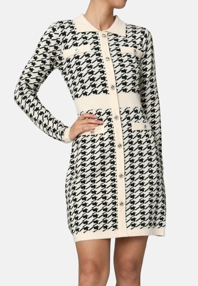 Femme portant une robe à manches longues en motif pied-de-poule noir et blanc avec des boutons sur le devant et des détails en crème au col et à la poche.