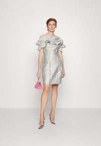Stříbrné šaty s odhalenými rameny, s volánkovým výstřihem, textured vzorem, přiléhavým střihem a horkorůžovou trojúhelníkovou kabelkou. Stříbrné vysoké podpatky.