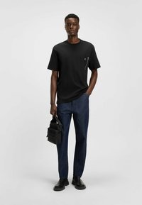 T-shirt nera a maniche corte con tasca con zip, abbinata a pantaloni in denim scuro e stivali neri. Piccolo logo sulla tasca.