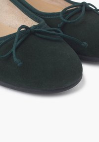 Bailarinas de ante verde con punta redonda, que presentan un acabado texturizado y un lazo decorativo en la parte frontal. Forro interior suave.