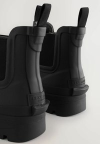 Schwarze Gummistiefel mit strukturierter Oberfläche, elastischen Seitenteilen, Zuglaschen und einer dicken, robusten Sohle. Verfügt über ein geprägtes Branding an der Ferse.