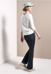 White long-sleeve shirt, dark flared jeans, mint green cap, and light sneakers with blue accents, displayed from the back.