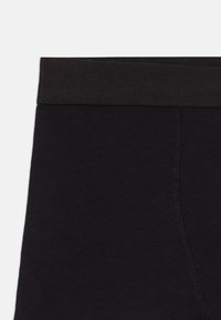 Schwarze Leggings mit einem weichen, elastischen Bund, die eine glatte Textur und ein einfaches Design aufweisen. Keine auffälligen Muster oder Akzente sichtbar.