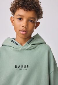 Zöld kapucnis pulóver, amelyen nagy fekete nyomtatott "BAKER" és "by TED BAKER" logó látható. Puha anyagból készült, laza fazonú, húzózsinóros kapucnival.