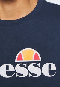 Sweat-shirt en coton bleu marine avec un grand logo blanc accompagné d'un graphisme multicolore : un demi-cercle jaune et rouge au-dessus du texte "esse."