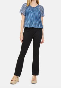 Modrá vzorovaná blůza s volným střihem, zkombinovaná s černými přiléhavými kalhotami a béžovými platformovými sandály. Průhledná, lehká tkanina.