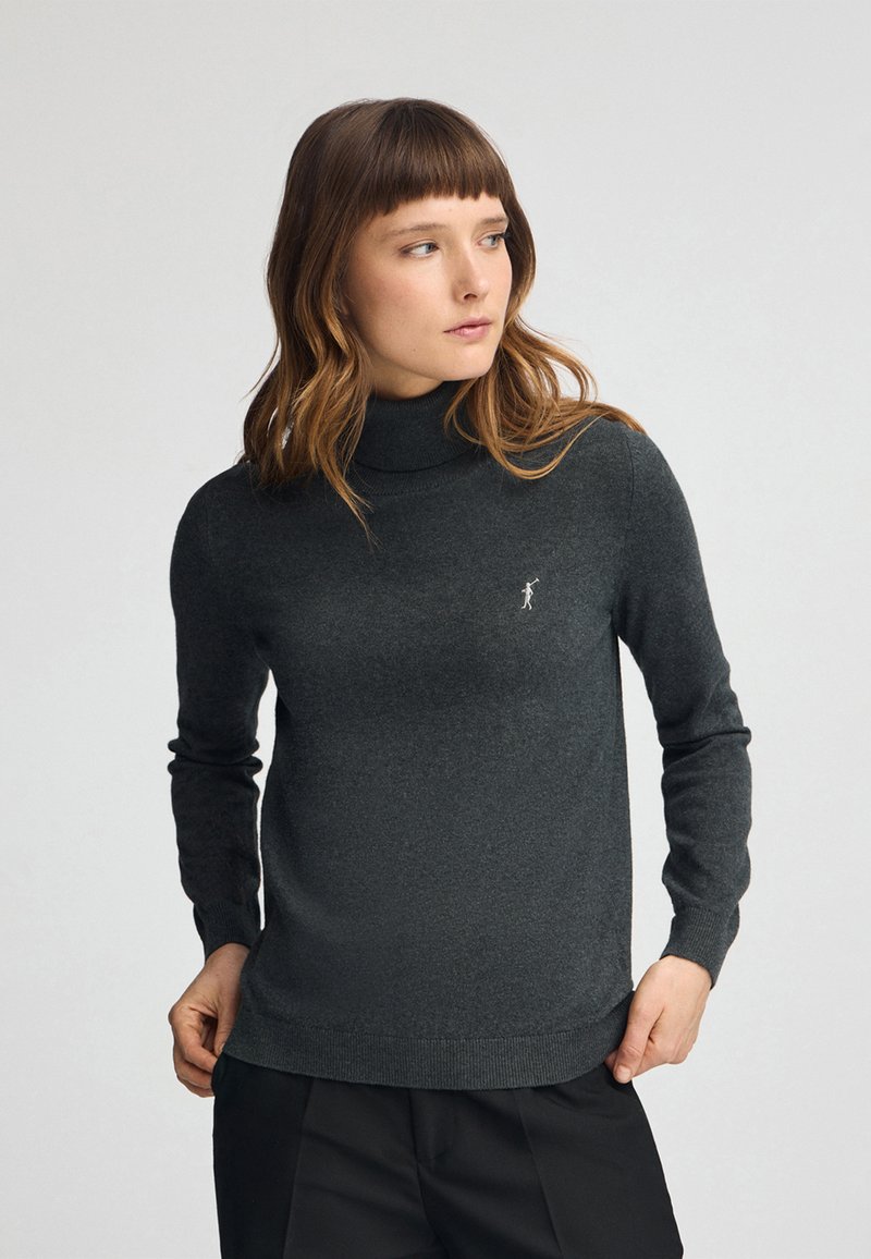 Pull en col roulé gris charbon en tricot doux. Il présente des manches longues, une coupe ajustée et un petit logo brodé sur la poitrine.
