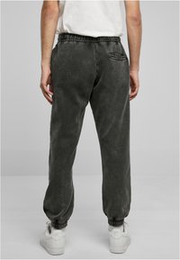 Mørkegrå joggebukser med elastisk talje og cuff, sidelommer og en børstet tekstur, parret med hvide sneakers.