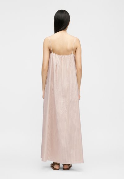 Ženska, gledana od zadaj, nosi dolgo, ohlapno brezrokavno roza obleko s tankimi navpičnimi črtami in rjave sandale.