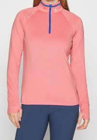 Dlouhý rukáv sportovní top v korálové barvě s půlzipem a modrým zipem. Obsahuje raglánové rukávy a hladký, elastický materiál.